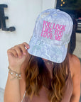 You Look Like You Love Me Camo Trucker Hat – Pink Lyrics Snapback worn by woman, featuring pink embroidered text on a gray camo background.