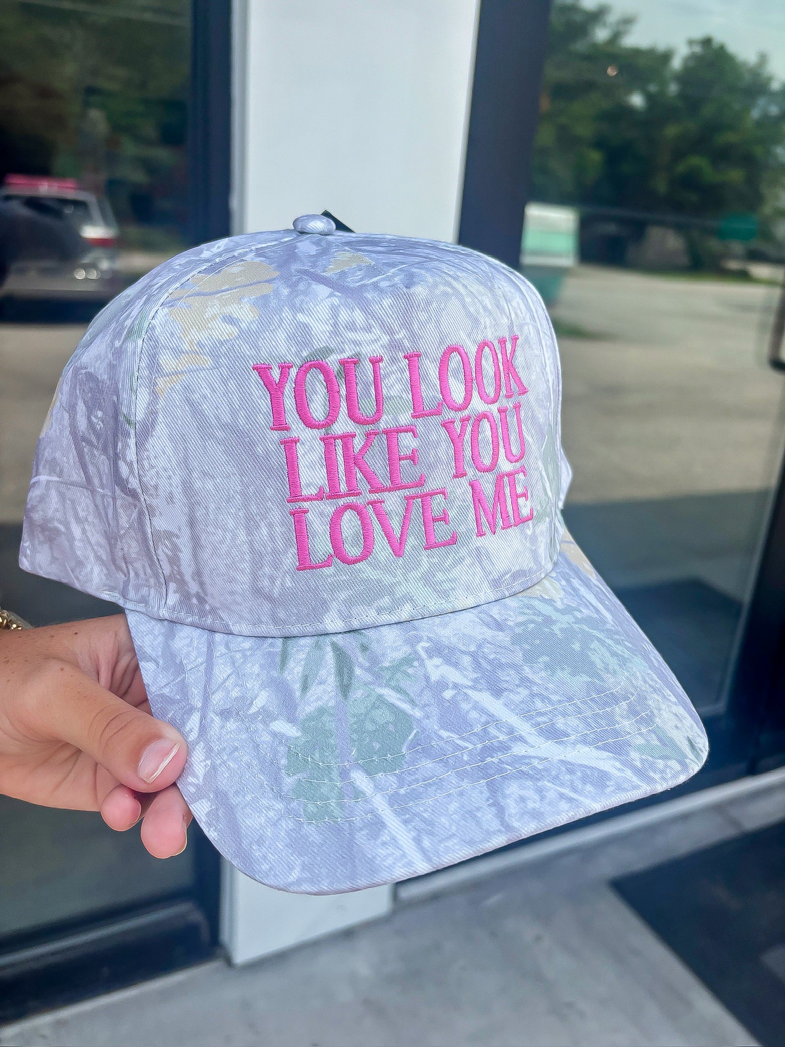 Close-up of You Look Like You Love Me Camo Trucker Hat with bold pink lyrics embroidery, adjustable snapback, and durable camo canvas.