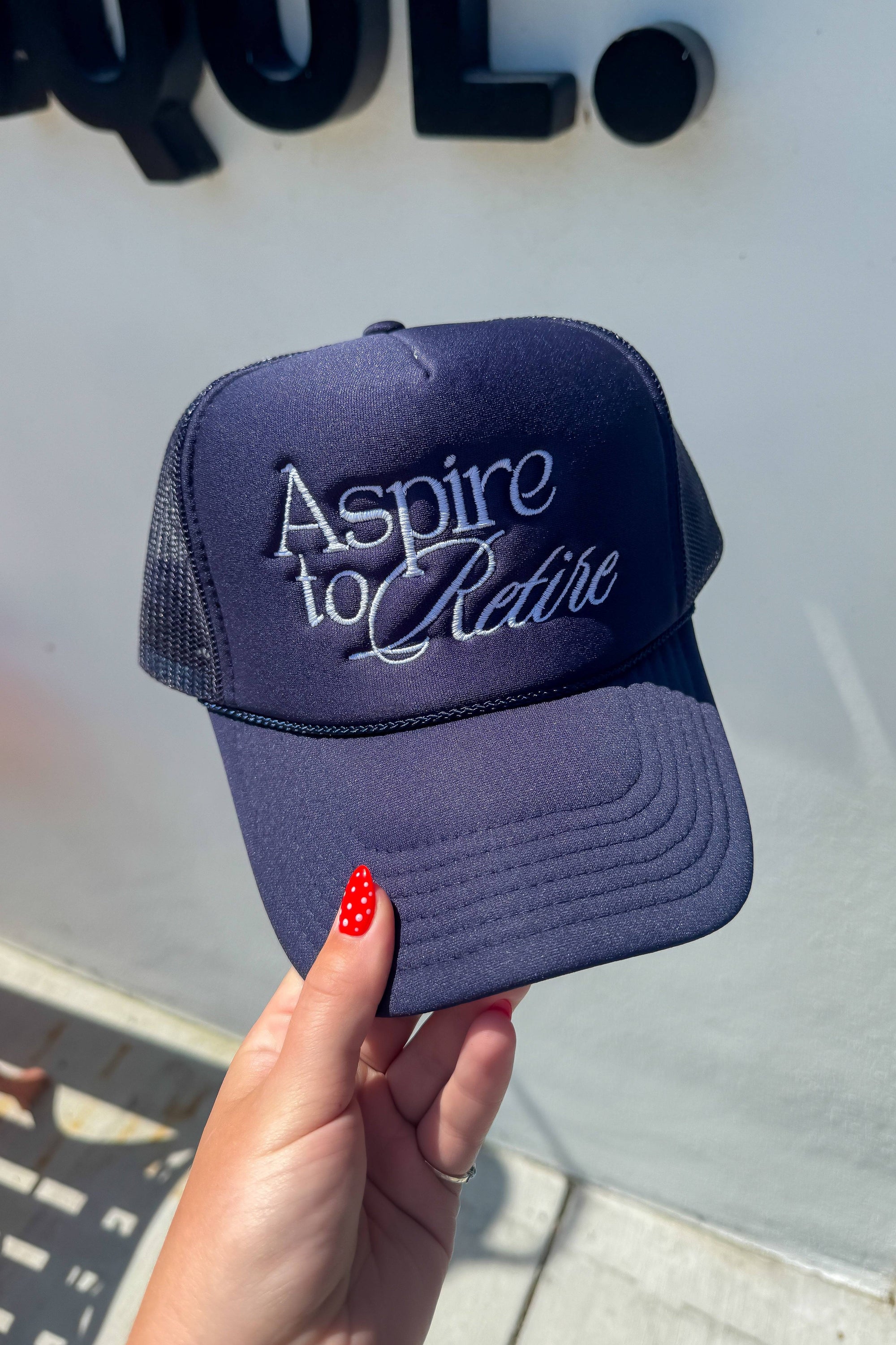 Close-up of Aspire to Retire Navy Trucker Hat – Foam & Mesh Snapback held by hand, showing detailed embroidery and breathable mesh back.