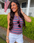 Woman in striped tank top and shorts standing in front of a house with an American flag.