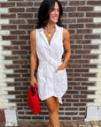 Woman in a white dress holding a red bag against a brick wall.
