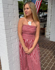 Woman in a red and white striped dress standing next to a white brick wall with an American flag in the background.