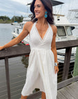 Woman in a white dress standing on a dock with boats in the background