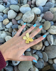 Golden Monarch gold butterfly ring worn on hand with blue nails, styled against natural stone background. Elegant adjustable butterfly ring for women.