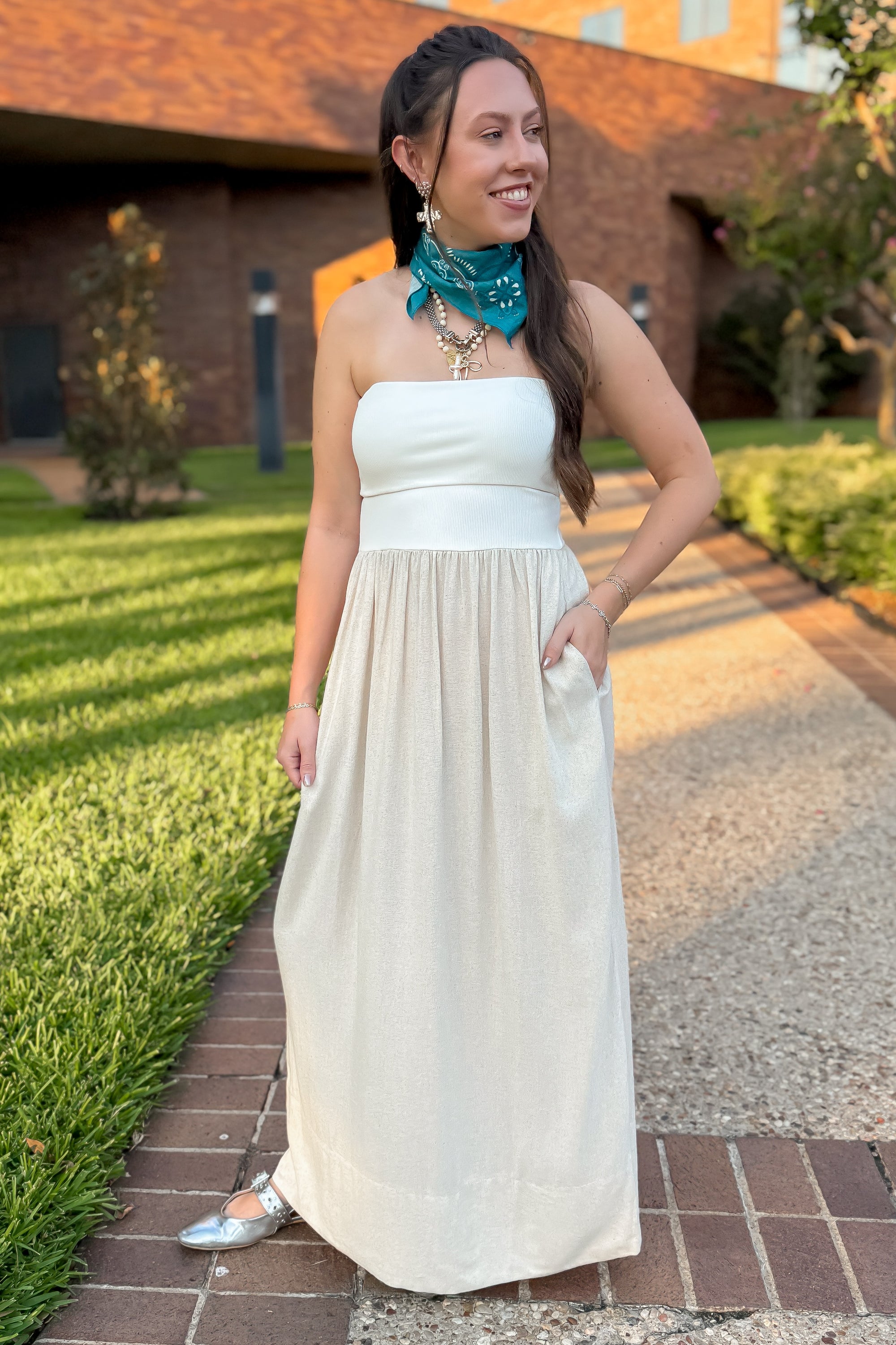 Oatmeal linen dress strapless and flowy, styled outdoors with silver flats and turquoise bandana for a casual summer look.