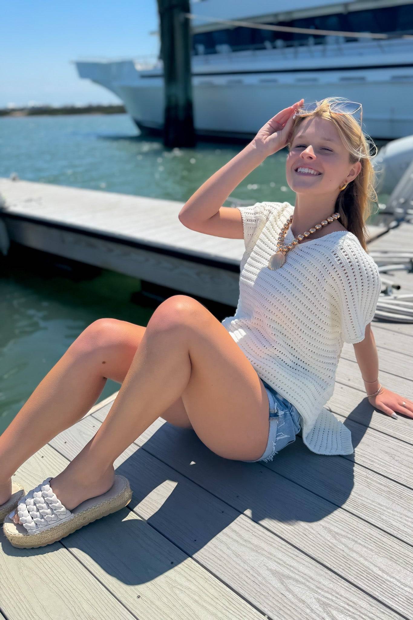 Effortless Elegance: White Open Knit Crochet Sweater styled with denim shorts, perfect for summer lounging by the harbor. Lightweight and breezy for vacay vibes.