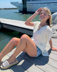 Effortless Elegance: White Open Knit Crochet Sweater styled with denim shorts, perfect for summer lounging by the harbor. Lightweight and breezy for vacay vibes.