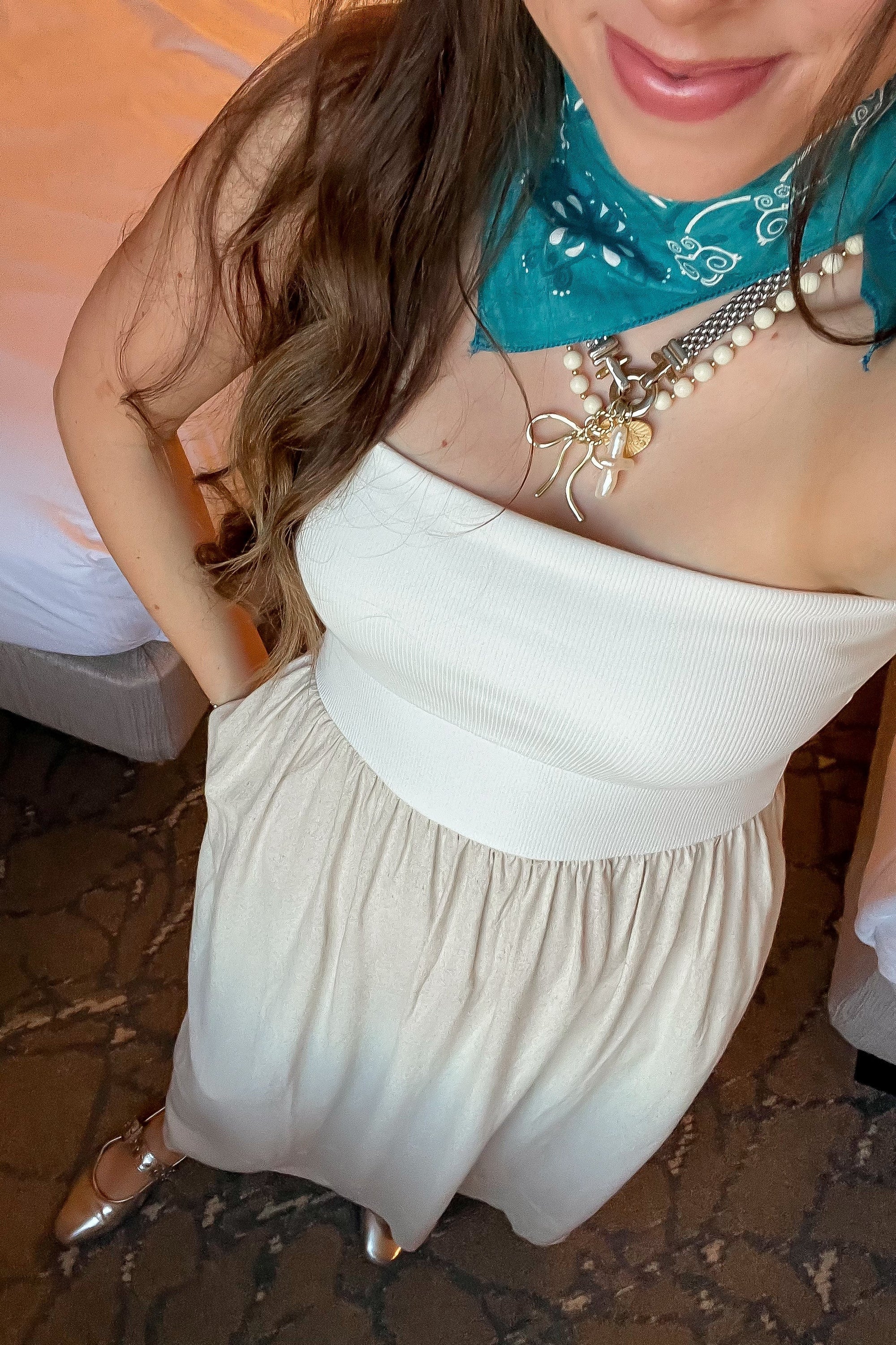 Close-up of strapless oatmeal linen dress with gathered waist, accessorized with layered necklaces and turquoise bandana scarf.