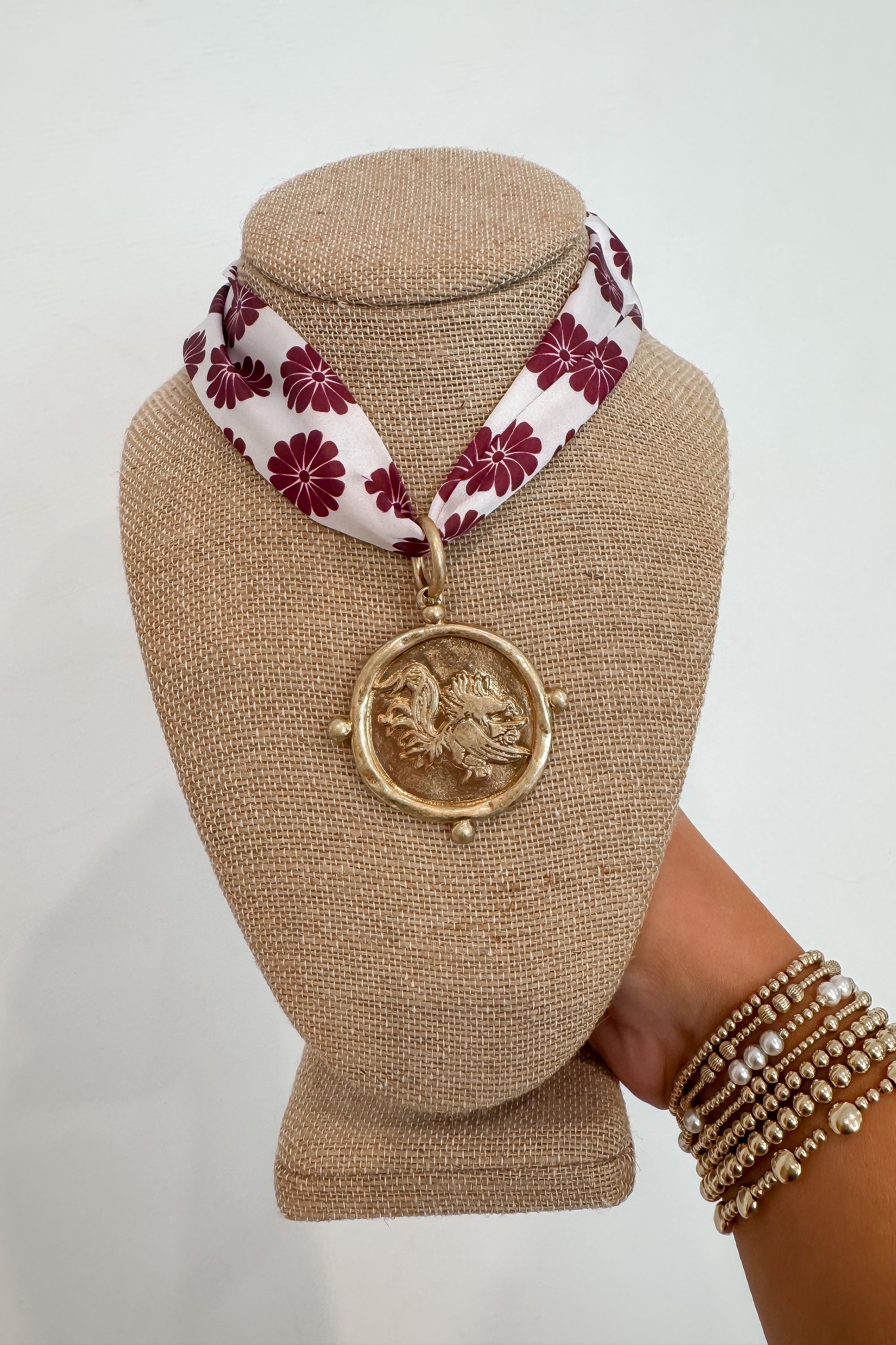 Garnet USC Gamecock Serafina Scarf Necklace from L. Mae Boutique featuring a gold medallion with Gamecock emblem on a floral garnet and white scarf.