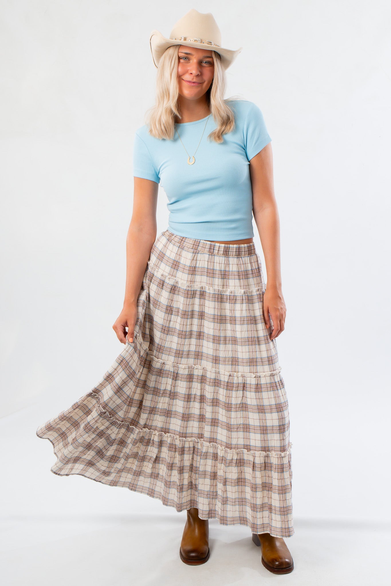 Model wearing Fort Worth Brown Plaid Maxi Skirt with light blue top and cowboy hat, showcasing western-inspired fall style.