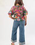 Back view of THML Printed Puff Sleeve V-Neck Top showing gathered detail and vibrant floral pattern, styled with cuffed denim jeans for a trendy look.