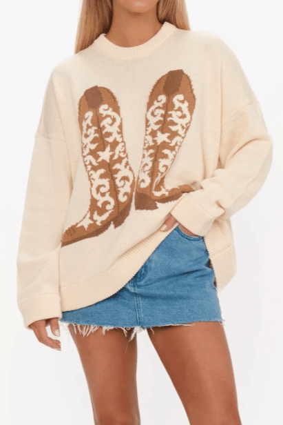 Front view of Show Me Your Mumu Cowboy Boot Knit Stay Awhile Sweater featuring bold cowboy boot graphic, worn with a frayed denim skirt for casual western style.