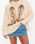 Front view of Show Me Your Mumu Cowboy Boot Knit Stay Awhile Sweater featuring bold cowboy boot graphic, worn with a frayed denim skirt for casual western style.