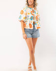 Model wearing a Spring Floral Tie-Front Top with short puff sleeves and a colorful floral pattern, paired with denim shorts and platform sandals.