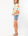 Side view of the Spring Floral Tie-Front Top showcasing its puff sleeves, peplum hem, and bright floral design, styled with casual denim shorts.