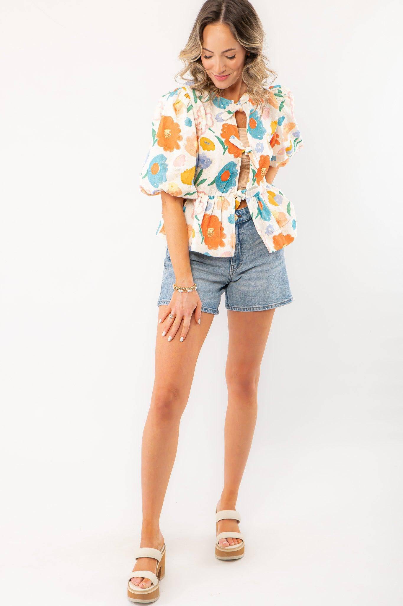 Model posing in a Spring Floral Tie-Front Top with a playful floral print, puff sleeves, and a relaxed fit, perfect for spring and summer styling.