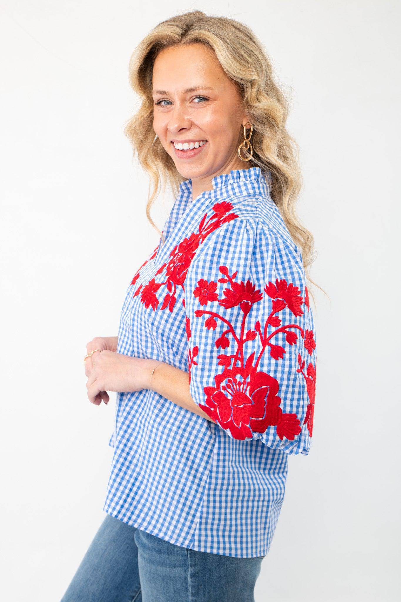 Side view of THML Blue Gingham Embroidered Top LM highlighting red floral embroidery on puff sleeves and a ruffled neckline, paired with denim jeans.