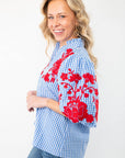 Side view of THML Blue Gingham Embroidered Top LM highlighting red floral embroidery on puff sleeves and a ruffled neckline, paired with denim jeans.