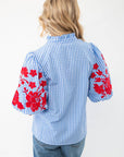 Back view of THML Blue Gingham Embroidered Top LM displaying puff sleeves with red floral embroidery and a ruffled neckline, styled with casual denim jeans.