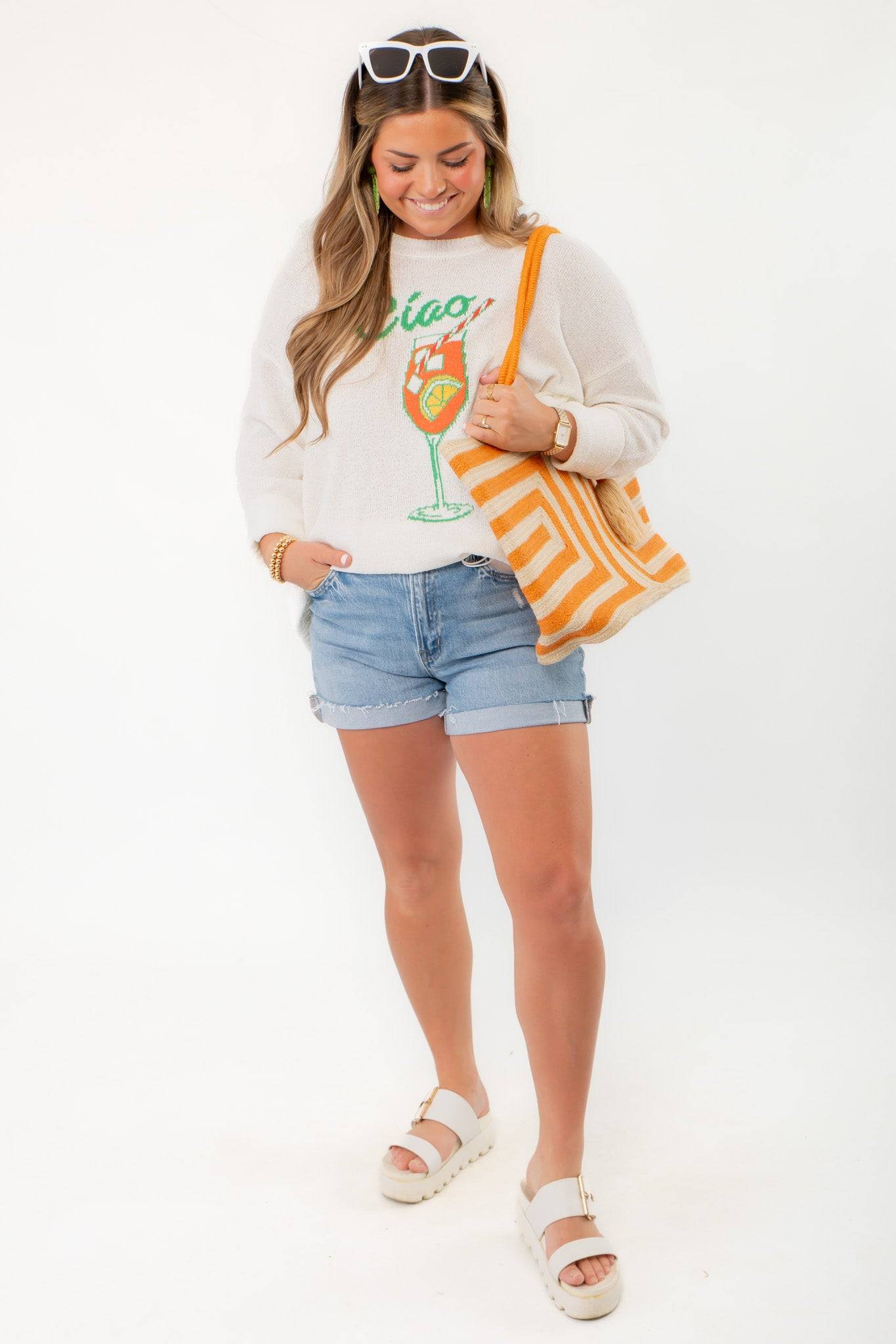 Model wearing Show Me Your Mumu Ciao Cocktail Woodsy Sweater with rolled denim shorts and accessories, showcasing cozy summer fashion.