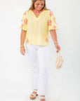 Model wearing THML Yellow Floral Pom Blouse paired with white jeans and platform sandals, ideal for a spring vacation outfit.