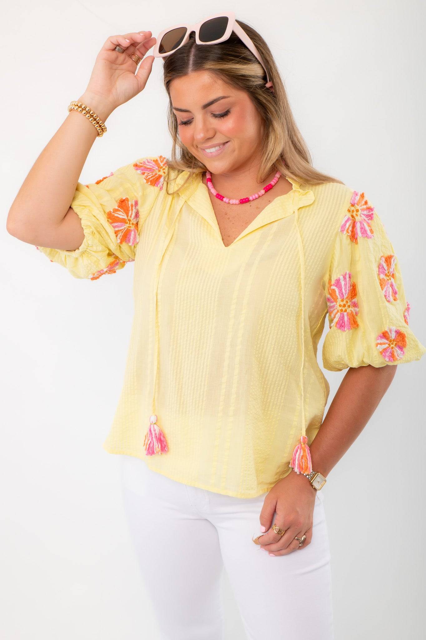 THML Yellow Floral Pom Blouse with pink tassels and puff sleeves, styled with white denim for a bright spring look.