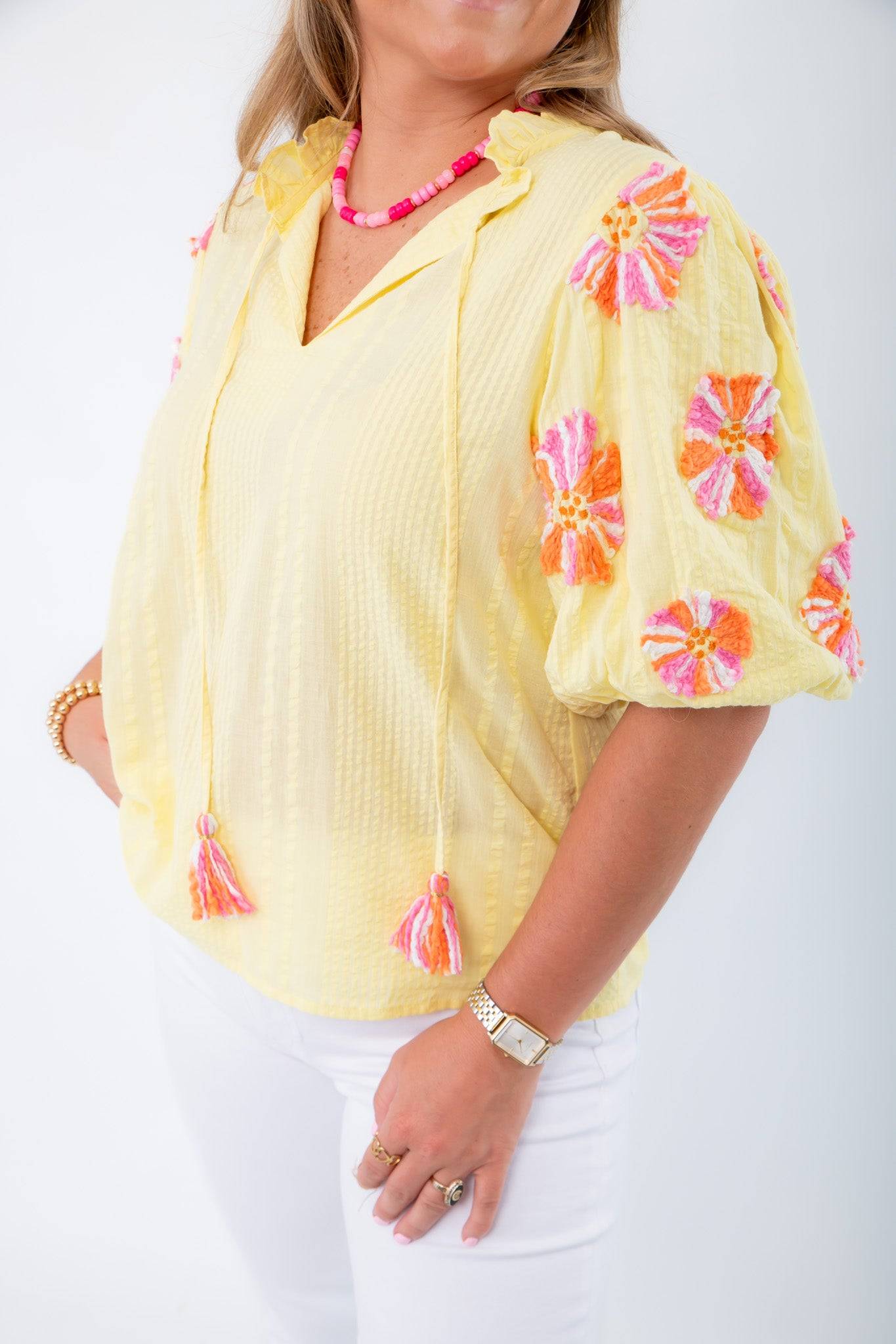 Close-up of THML Yellow Floral Pom Blouse featuring textured fabric and vibrant pink-orange floral embroidery on sleeves.