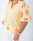 Close-up of THML Yellow Floral Pom Blouse featuring textured fabric and vibrant pink-orange floral embroidery on sleeves.