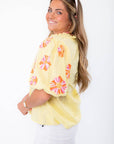 Side view of THML Yellow Floral Pom Blouse showing puff sleeves with floral embroidery and relaxed fit for casual elegance.