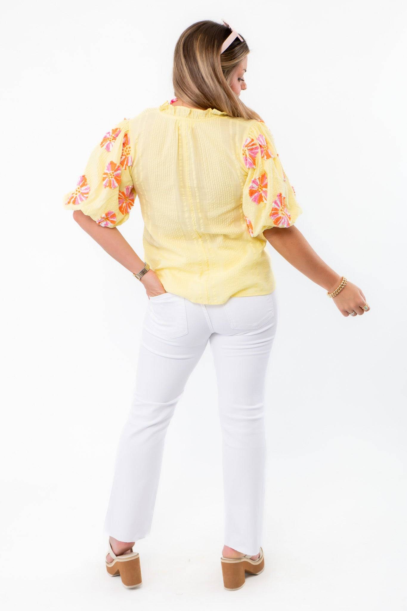 Back view of THML Yellow Floral Pom Blouse highlighting lightweight fabric and colorful sleeve details, styled with white denim.