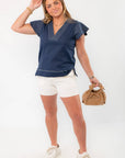 Model wearing THML Navy Ruffle Sleeve Top with striped ruffle sleeves and white shorts, perfect for a harbor chic summer ensemble.