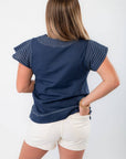 Back view of THML Navy Ruffle Sleeve Top featuring stitched detailing and flutter sleeves, paired with white shorts for a coastal vibe.
