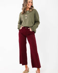 Model wearing Kut Maroon Meg High Rise Jeans with wide leg silhouette and raw hem. Ideal for holiday styling with heels or boots.