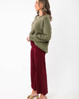 Side profile of the Martini A Day Olive Beaded Sweater styled with burgundy pants. A festive and comfy top for seasonal fashion.