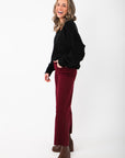 Side view of Olivia Oversized Black V‑Neck Sweater showing soft knit texture and loose fit, styled with burgundy pants and heeled boots.