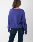 Back view of Olivia Oversized Purple V‑Neck Sweater highlighting ribbed hem and oversized cut in breathable knit fabric.
