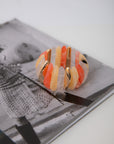 Stretchy Orange Wide Stone Bracelet resting on fashion magazine, highlighting bold summer colors and gold detailing in statement jewelry design.