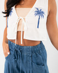 Close-up of MinkPink Isadora Embroidered Top featuring tie-front closure and detailed blue palm embroidery on white fabric.