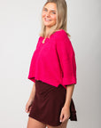 Side view of Fuchsia Short Sleeve Crop Sweater – Oversized pink knit top with relaxed fit and short sleeves, paired with a burgundy skirt.