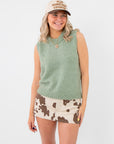 Mila Desert Sage Green Knit Sleeveless Sweater with crew neck, styled with cow print mini skirt and beige cap. Soft green knit top for layering.