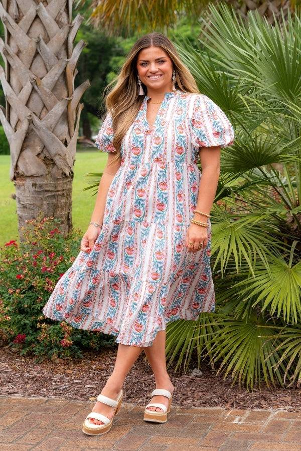 THML Pink & Cream Floral Print Midi Dress with puff sleeves and v-neckline, styled for summer elegance in a garden setting.