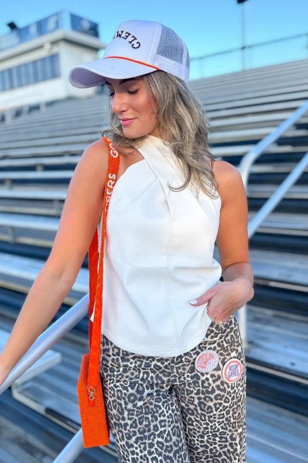 On Time Ecru Faux Leather Top with halter neck design styled for gameday with leopard pants and orange accessories in stadium setting.