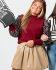 THML Mixed Media Garnet Top with patterned knit sleeves styled with beige pleated skirt and brown boots. Versatile fall knit shirt for casual wear.