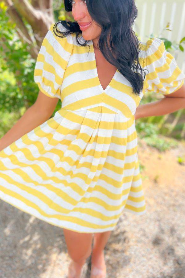 Close-up of Sweetest Surprise Yellow V Neck Mini Dress showcasing yellow and white stripes, puff sleeves, and flattering pleated waistline.