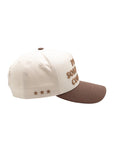 Side view of Play Something Country Trucker Hat showing embroidered stars and structured cream crown with brown curved brim.