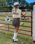 Back view of Show Me Your Mumu Cowboy Boot Knit Stay Awhile Sweater draped over shoulders, paired with a brown mini dress and white cowboy boots for a western-inspired outfit.