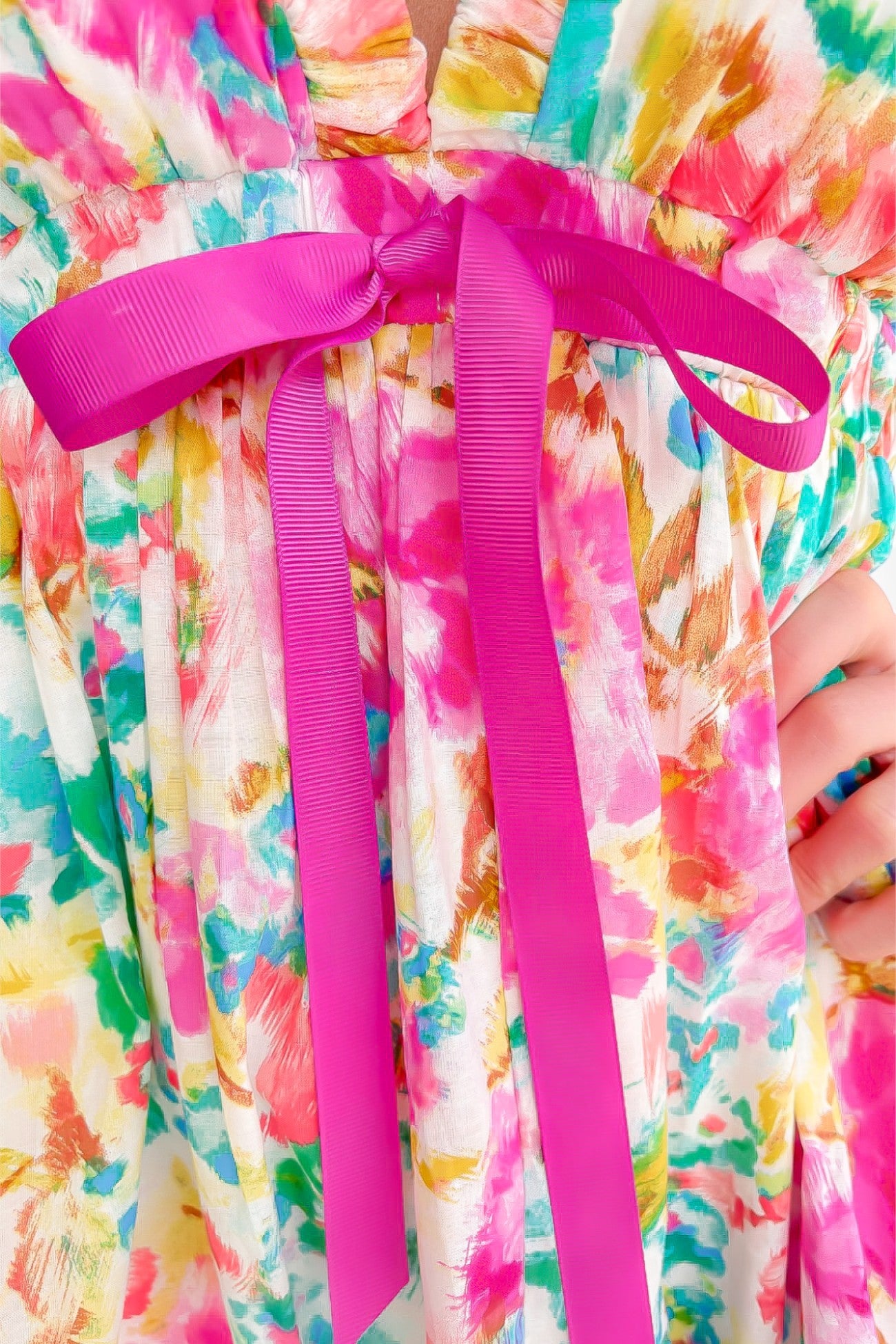 Close-up of the Meet Me in Santorini Aegean Garden Dress showcasing the pink ribbon tie detail. Colorful floral pattern enhances its feminine charm.