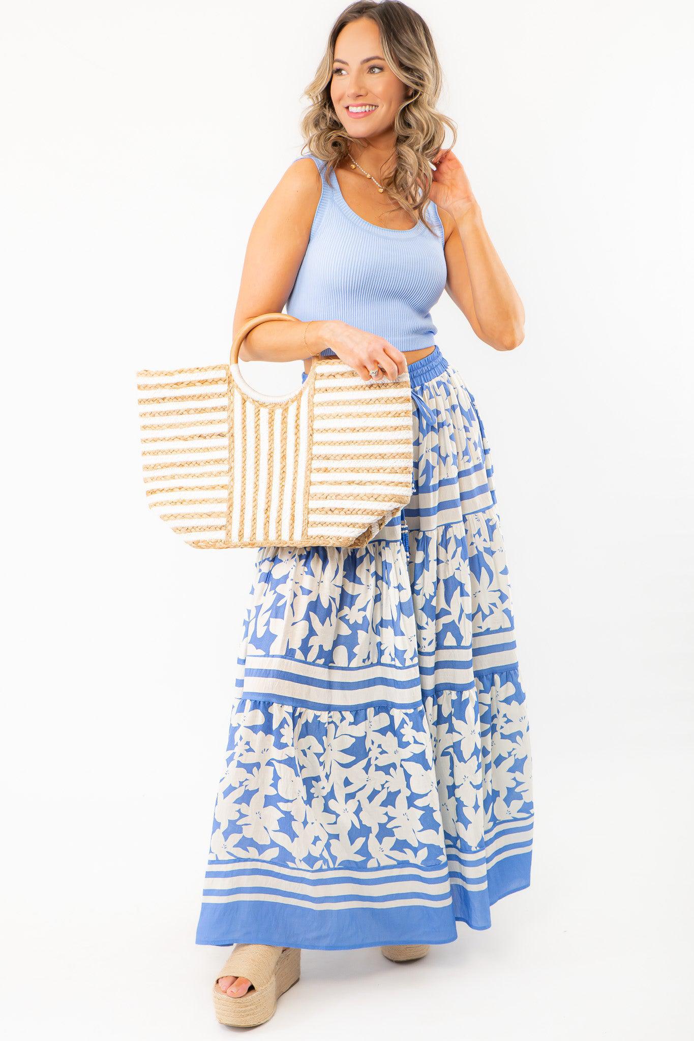 Boho chic bright blue floral print tiered maxi skirt paired with a woven straw bag and blue tank top, perfect for summer vacations.