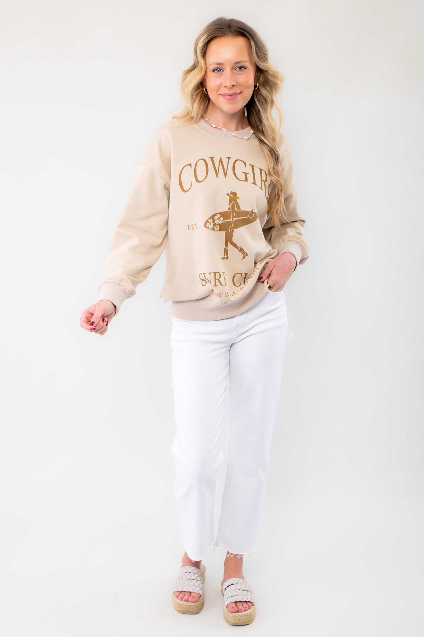 Model wearing the Cowgirl Surf Club Graphic Sweatshirt paired with white jeans and woven sandals. A casual yet stylish look perfect for summer layering.