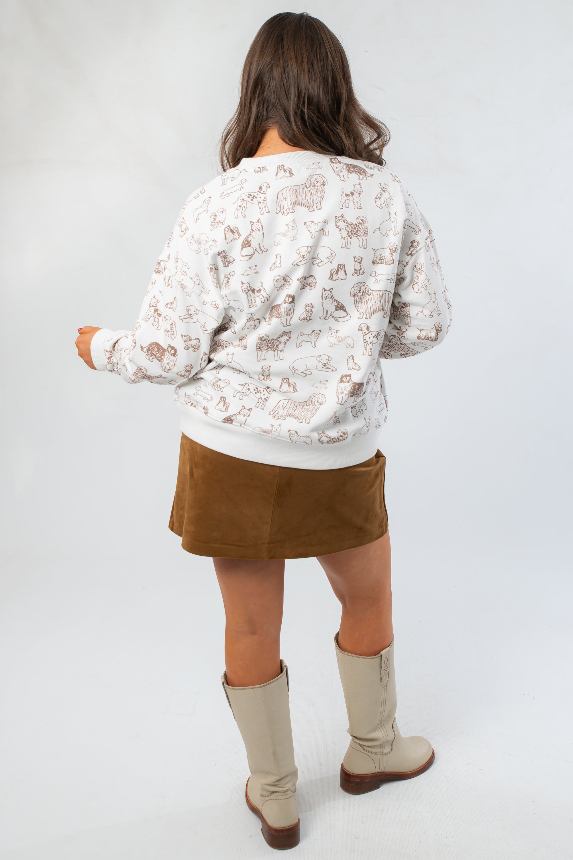 Back view of Snuggle Pup Dog Print Sweatshirt featuring all-over brown puppy illustrations on a white crewneck, paired with a suede mini skirt.